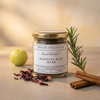 Jar of Ardah Organics hibiscus hair mask with an apple, rosemary, and cinnamon on a neutral background