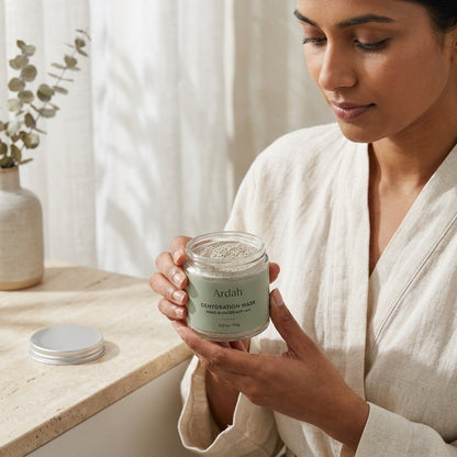 Woman holding a jar of Ardah Purification Mask in a bathroom setting
