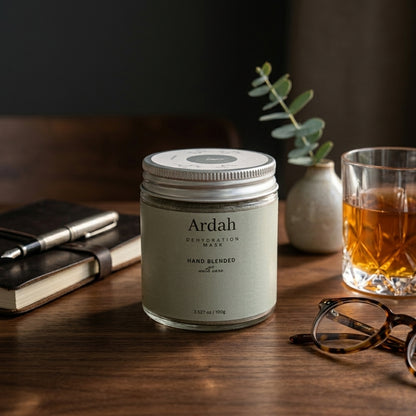 Ardah dermafoliant mask jar on a wooden surface with a glass of tea, notebook, and glasses.